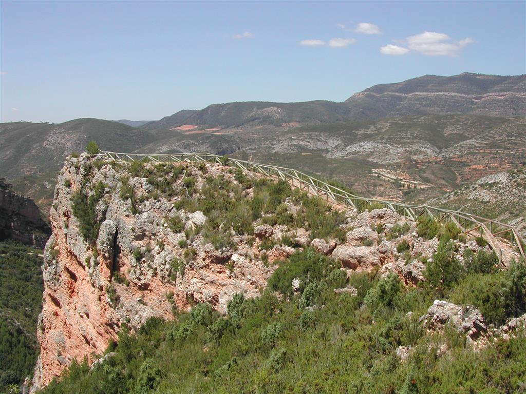 (676.085, 4.382.773). Vista hacia el suroeste del recorrido por la cresta rocosa de conglomerados terciarios desde la parada III-2 a la parada III-1. Al fondo, bloques tectónicos levantados y hundidos de la fosa de Chera (gris Cretácico y rojizo Terciario).