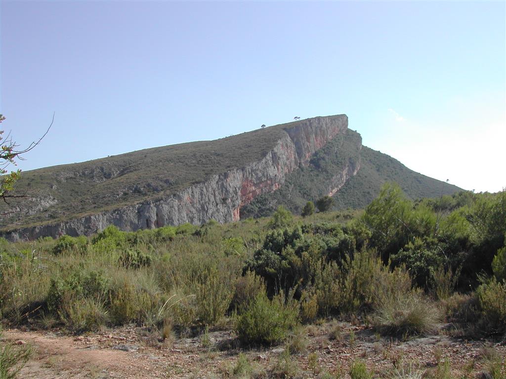 (679.805, 4.392.690; ETRS89 y huso 30). Panorámica del cerro de Los Calderones (La Punta) y el cortado del cañón del río Turia en el entorno del embalse de Loriguilla. El relieve estructural y escarpe están formados en la Fm Higueruelas, y la ladera vertiente hacia el embalse de Loriguilla (hacia la derecha) está formada en la Fm Loriguilla.