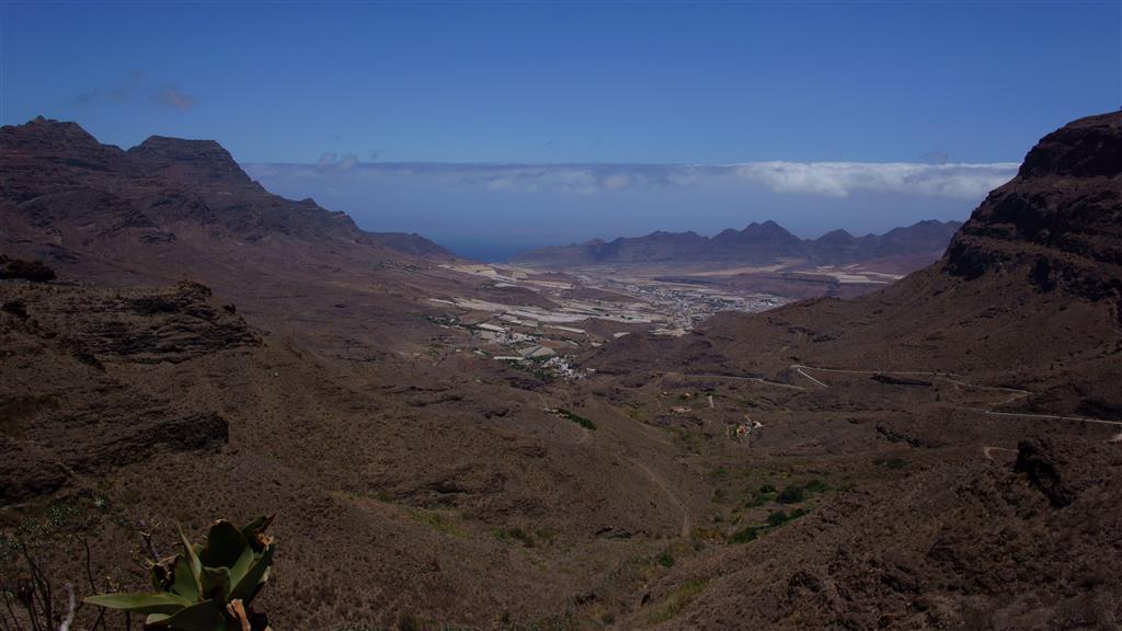 El valle de La Aldea desde el Sureste. Al fondo se abre la playa. La panorámica muestra una cuenca cerrada por montañas que definen un circo. La cuenca es atravesada por el cauce en dos puntos: el canal intermedio y la desembocadura. La cuenca recibe las aguas de toda la cumbre y las drena por la desembocadura.