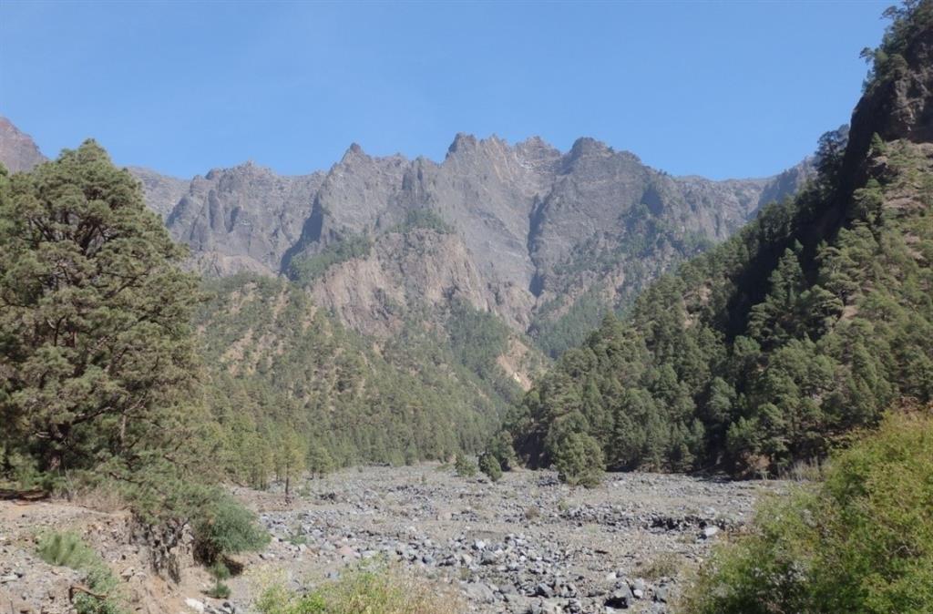 En primer plano los depósitos torrenciales actuales de bloques y cantos de la Playa de Taburiente en la zona de acampada del Parque Nacional. En ambos márgenes se disponen las terrazas del Holoceno superior. Al fondo la pared de la Caldera, en segundo plano el Roque Salvaje. Año 2020