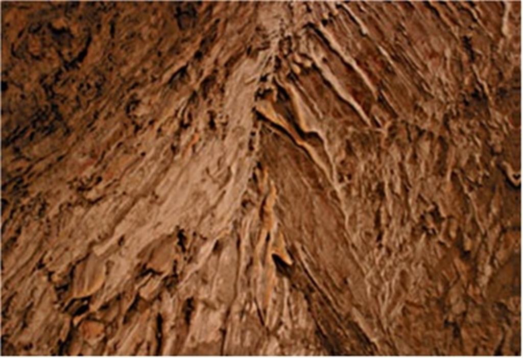 Techo de la cueva, condicionado por la intersección de dos fallas normales de vergencias opuestas. Obsérvese en la oriental, la existencia de mineralizaciones rojas de hierro y de espeleotemas lineales que se adaptan a las estrías de la falla, sin separarse de la pared