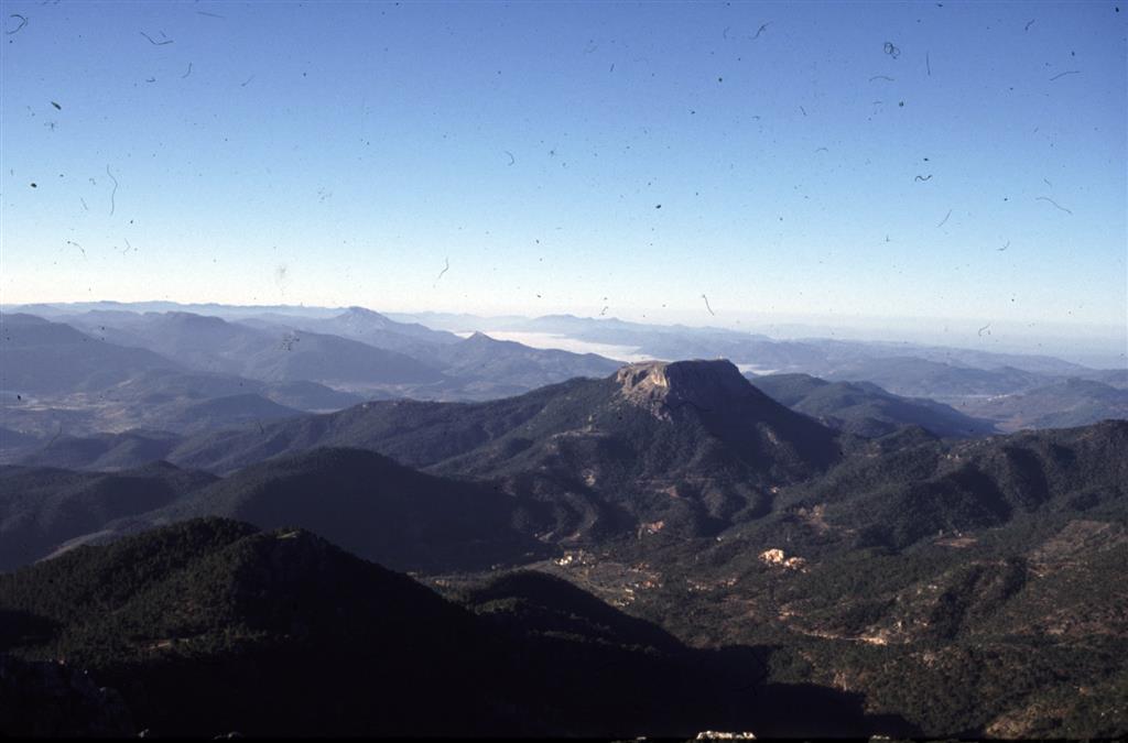 X: 541.338 Y: 4.261.527  Panorámica hacia el sur desde el Pico de la Sarga. El Cerro plano que aparece en la mitad de la imagen es el Cambrón formado en su parte más alta por dolomías del Cenomaniense y calizas del Senoniense. Más al fondo se encuentran los relieves de la Bucentaina y Peñalta. El valle en el que se encuentran las nubes bajas es el Valle de Hornos